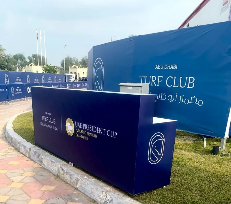 Branded reception counter with blue event graphics installed by Evolution Furniture at Abu Dhabi Turf Club.